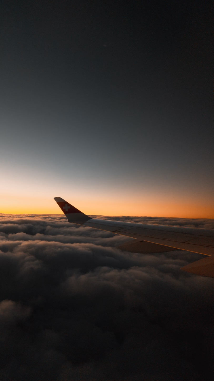 Airplane wing above clouds at sunset